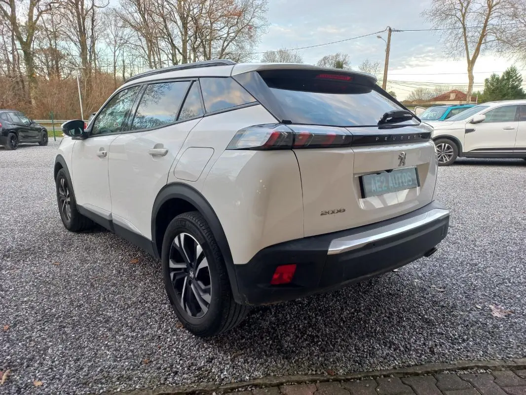 Peugeot 2008 blanc vue 3/4 arrière droit, jantes alliage noires, vitres teintées et toit noir contrasté.