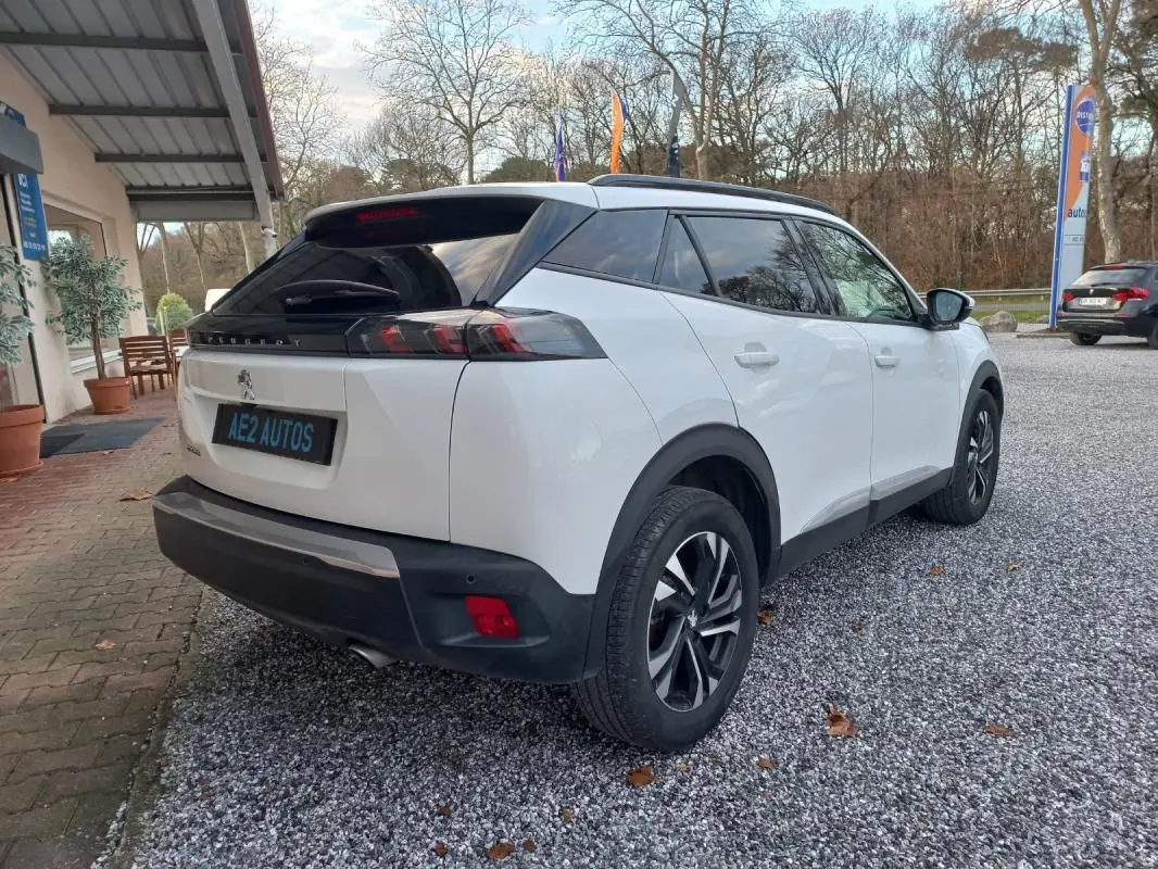 Peugeot 2008 blanc vue 3/4 arrière droit avec jantes alliage et toit noir dans un parking extérieur.