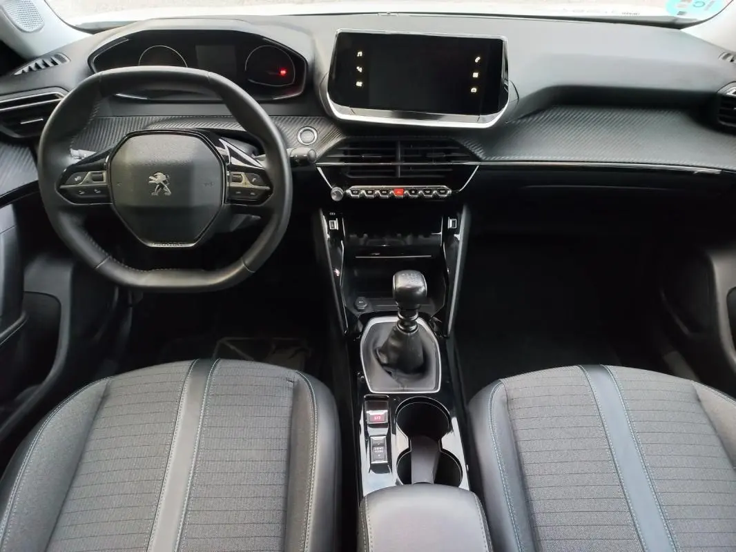 Vue intérieure avant du Peugeot 2008 blanc 2021, tableau de bord moderne avec écran tactile et boîte manuelle.