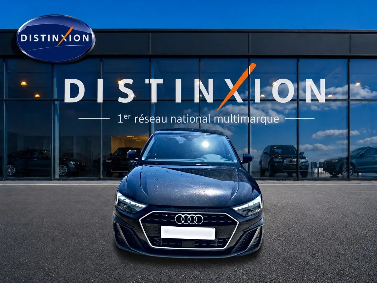 Audi A1 Sportback noir vue de face, stationnée devant une vitrine avec logo Distinxion en arrière-plan.