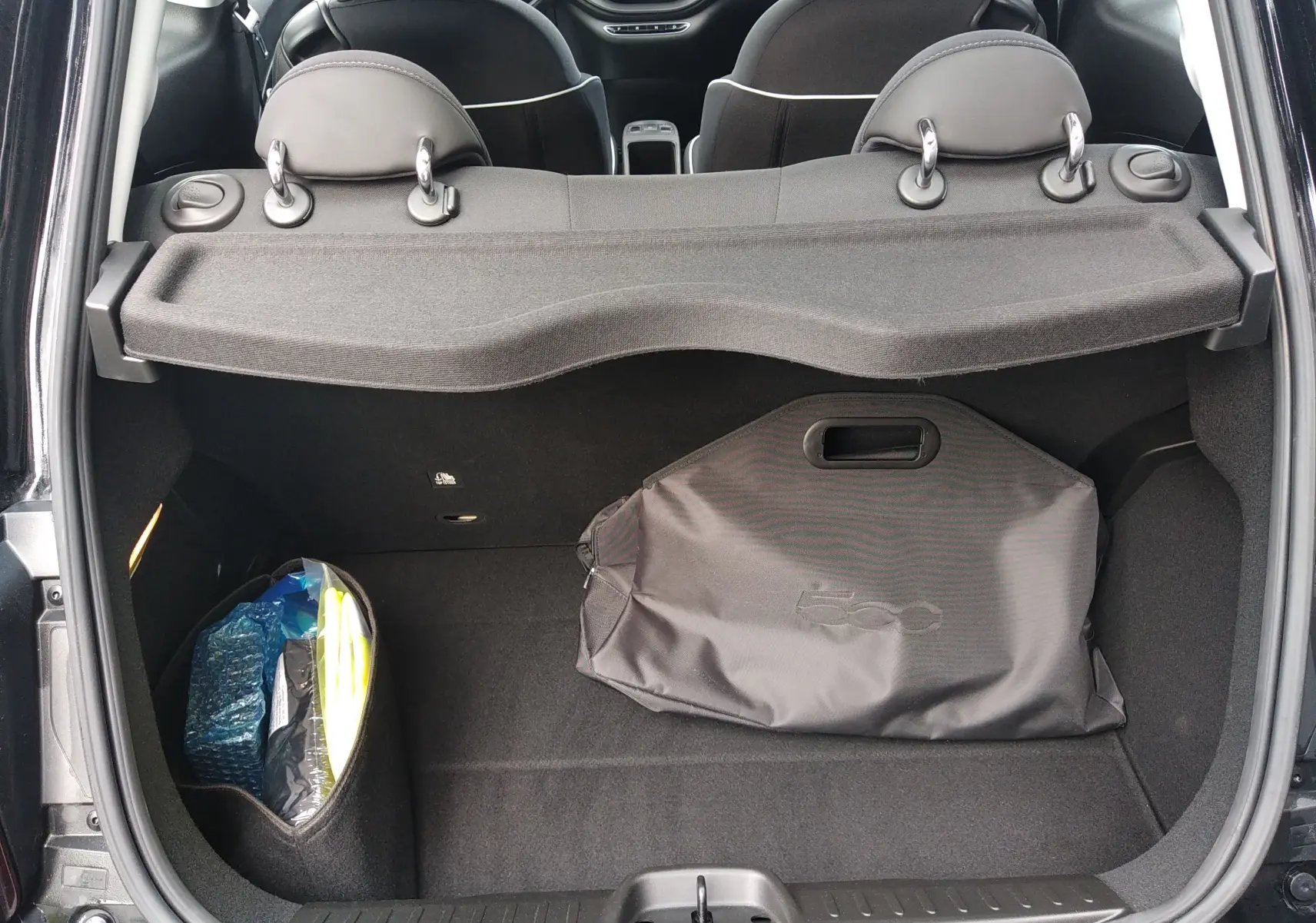 Vue arrière du coffre ouvert d'une FIAT 500 électrique noire 2024, avec housse et rangement latéral visible.