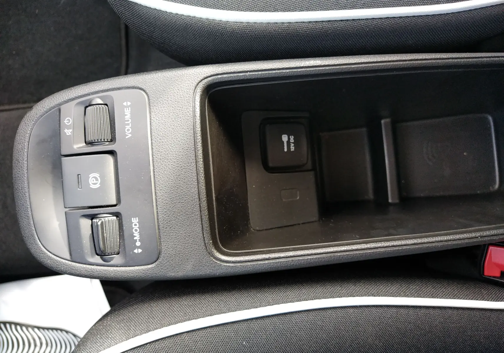 Vue plongeante sur la console centrale noire de la Fiat 500 électrique 2024, avec commandes volume et mode, prise 12V visible.