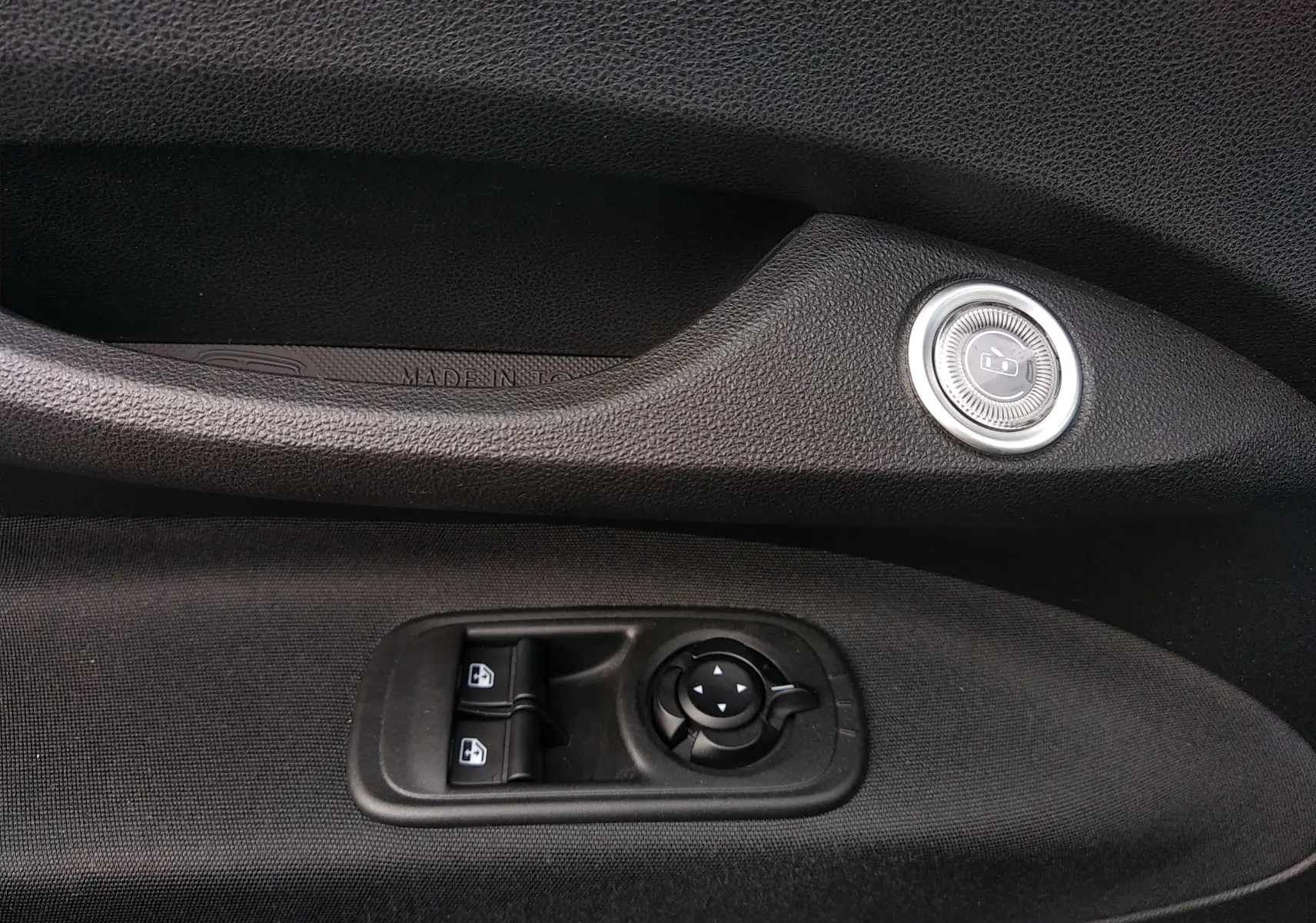 Détail intérieur côté gauche de la porte noire de la Fiat 500 électrique 2024 avec commandes de vitres et rétroviseurs.