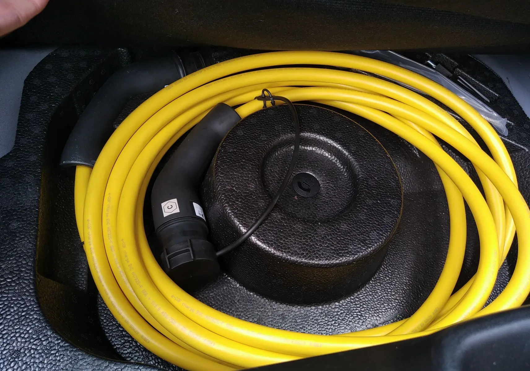 Câble de recharge électrique jaune enroulé dans le coffre d'une Fiat 500 électrique noire 2024.