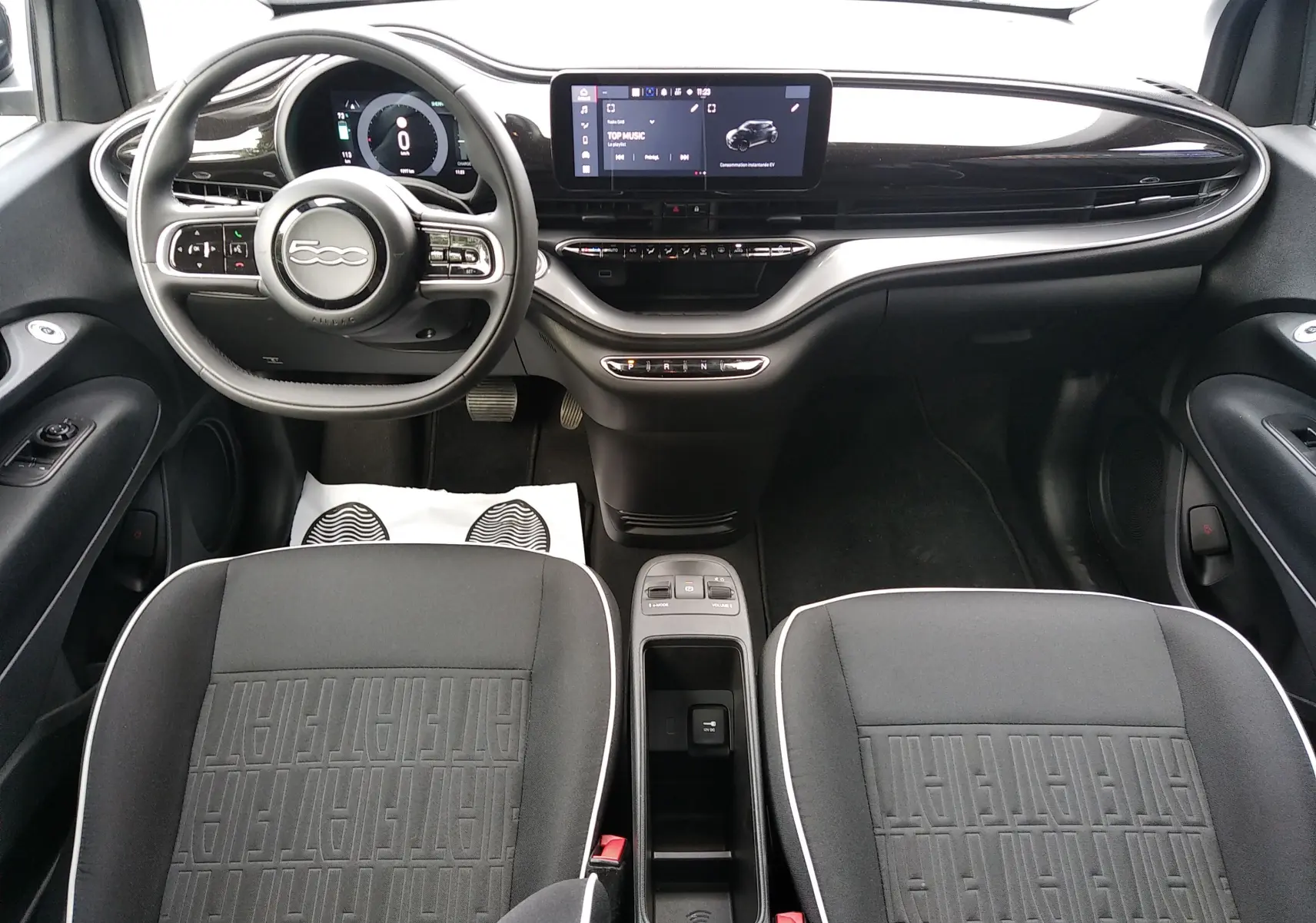 Vue intérieure avant de la Fiat 500 électrique noire 2024, avec tableau de bord moderne et sièges tissu noirs à logo Fiat.