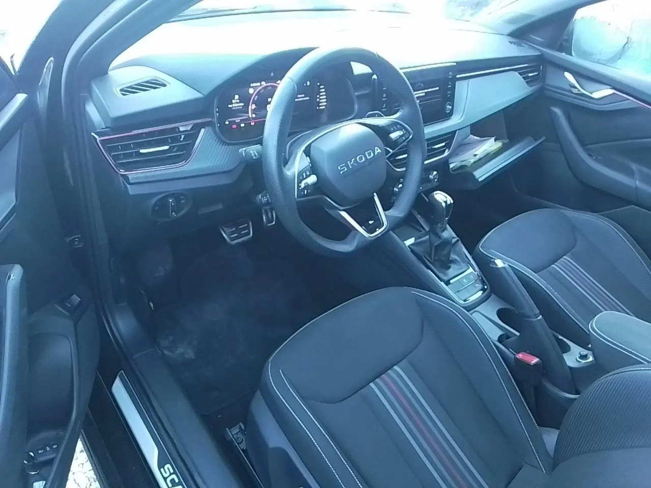 Vue intérieure côté conducteur de la Skoda Scala Monte-Carlo 2025, sellerie noire avec bandes rouges et volant multifonctions cuir.