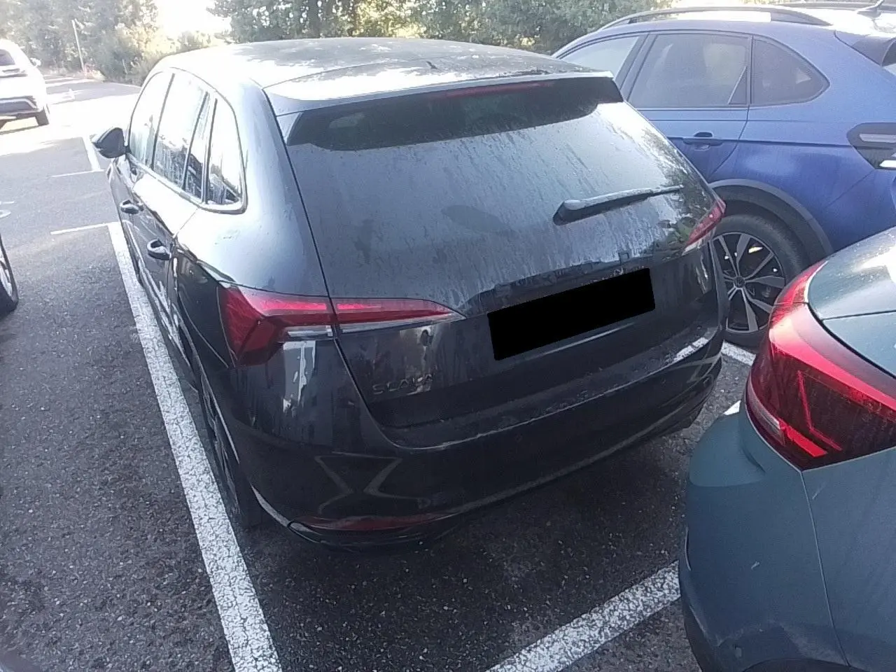 Vue 3/4 arrière d'une Skoda Scala noire Magic avec hayon électrique, stationnée entre deux véhicules.