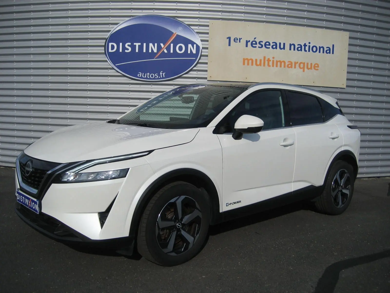 Nissan Qashqai blanc en 3/4 avant droit, avec jantes bi-ton noires et logo e-power sur la portière.