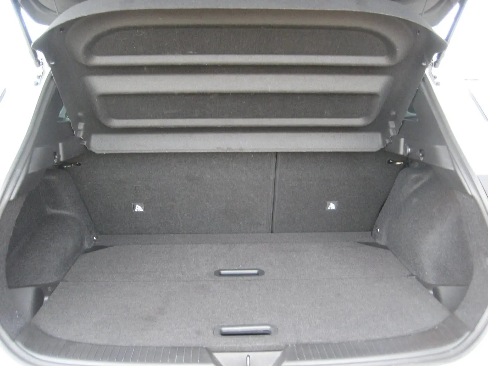 Coffre ouvert d'un Nissan Qashqai blanc 2024, vue arrière montrant l'espace de chargement vide et la moquette grise.