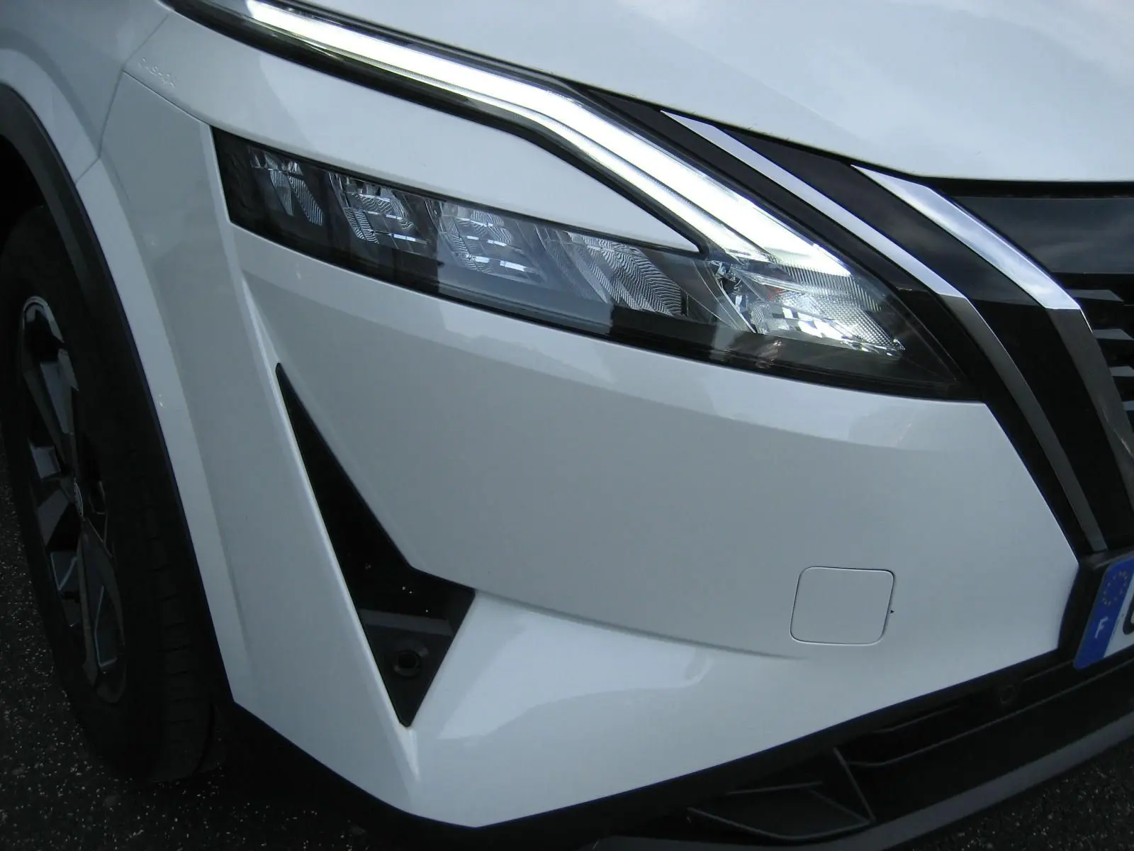 Gros plan sur l'avant gauche blanc du Nissan Qashqai 2024, mettant en valeur le phare LED et la calandre noire.