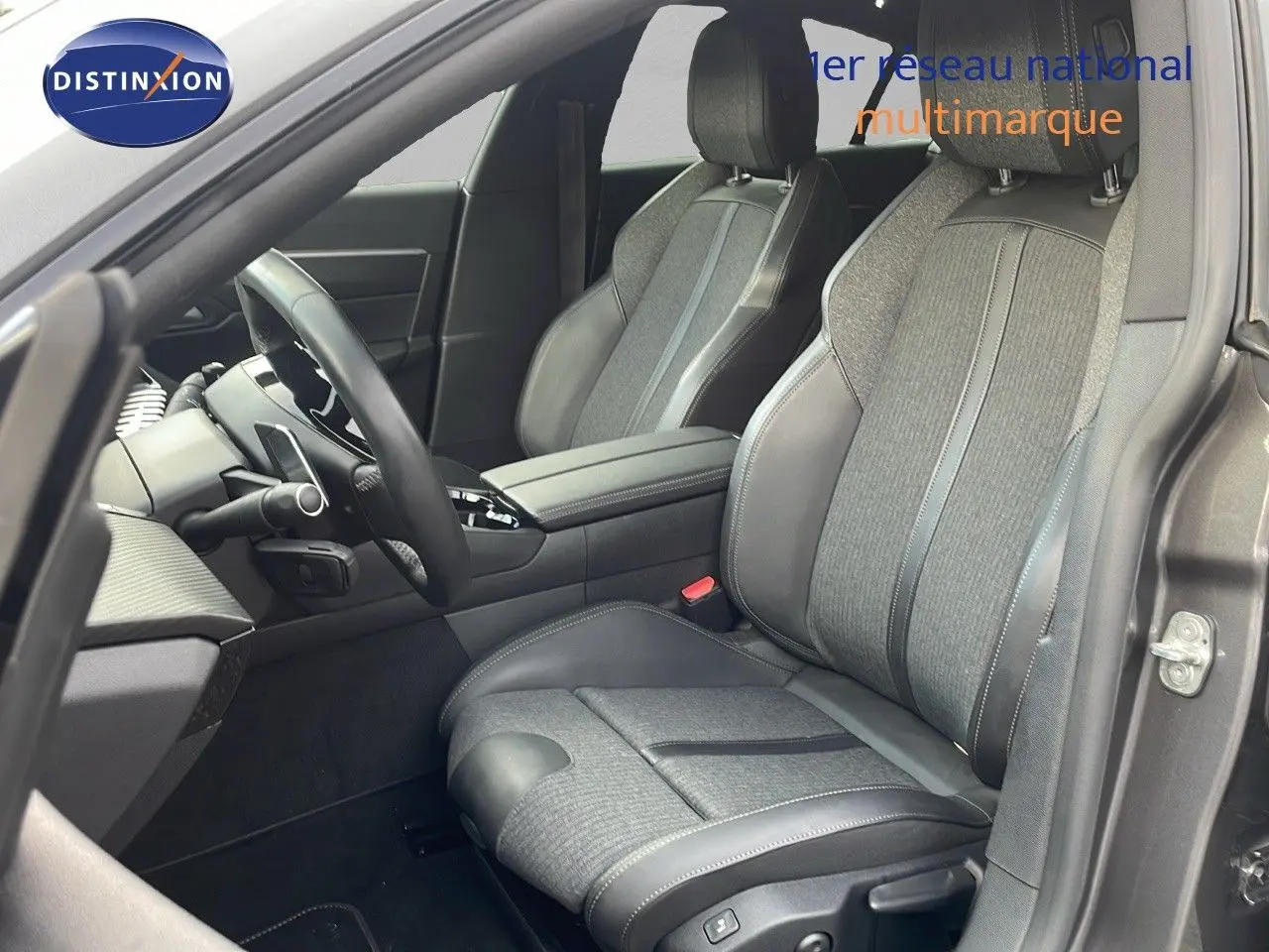 Vue intérieure côté conducteur de la Peugeot 508 gris platinium, sièges cuir et tissu noir avec console centrale visible.