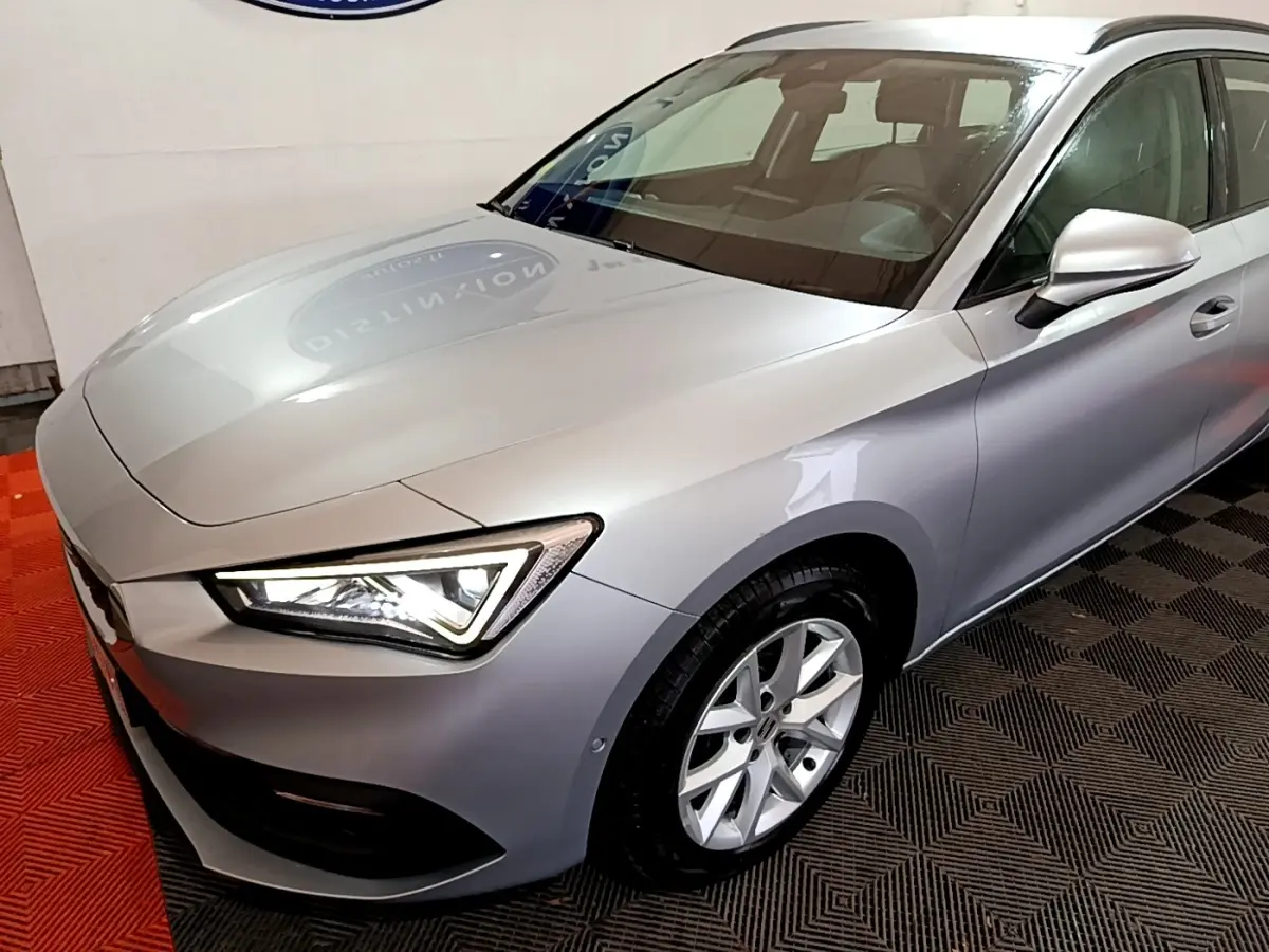 Vue 3/4 avant droit d'une SEAT LEON gris clair avec phares LED et jantes alliage visibles.