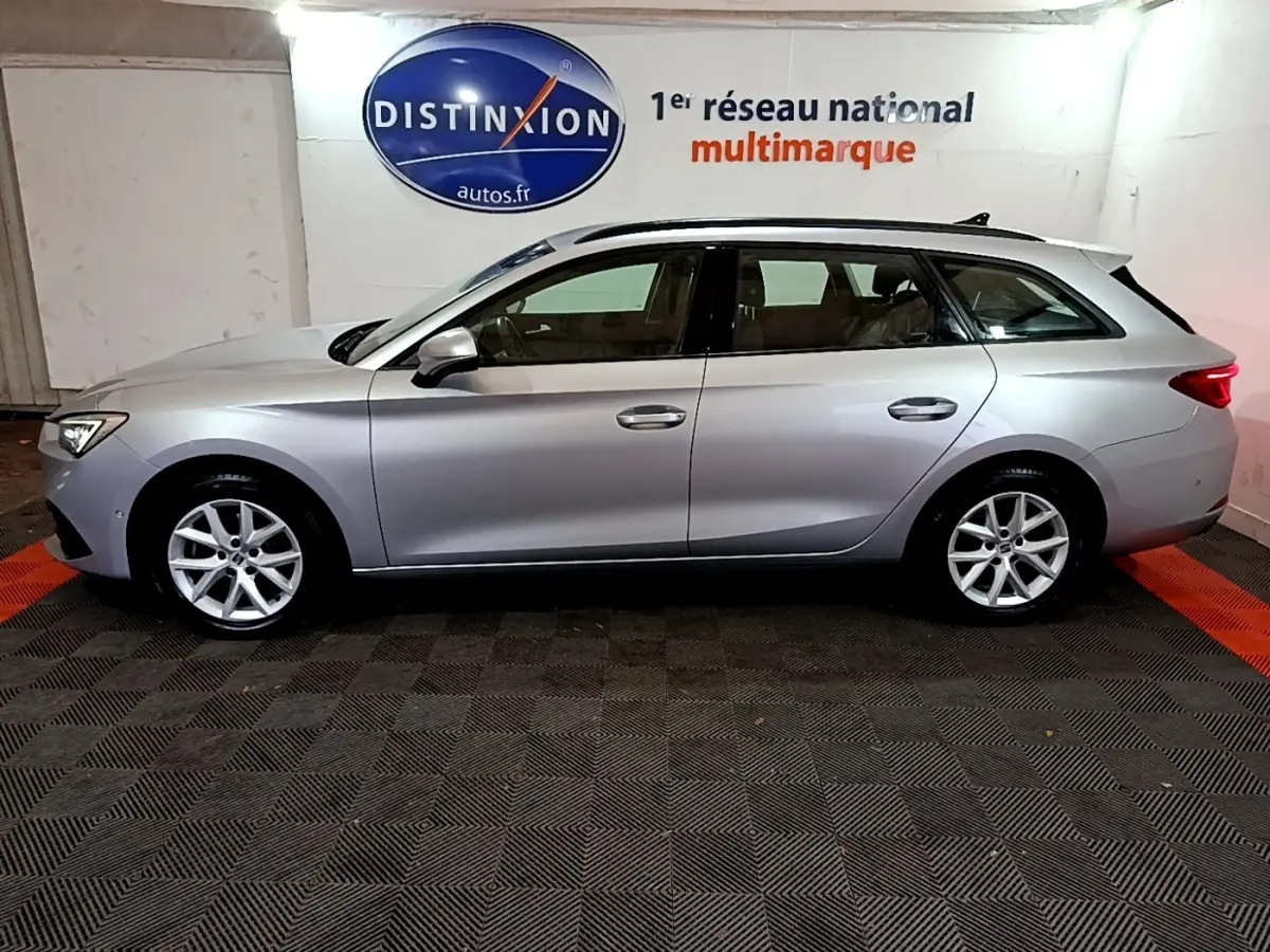 Profil côté gauche d'une SEAT LEON gris clair break 2022, roues alliage et rails de toit noirs visibles en intérieur showroom.