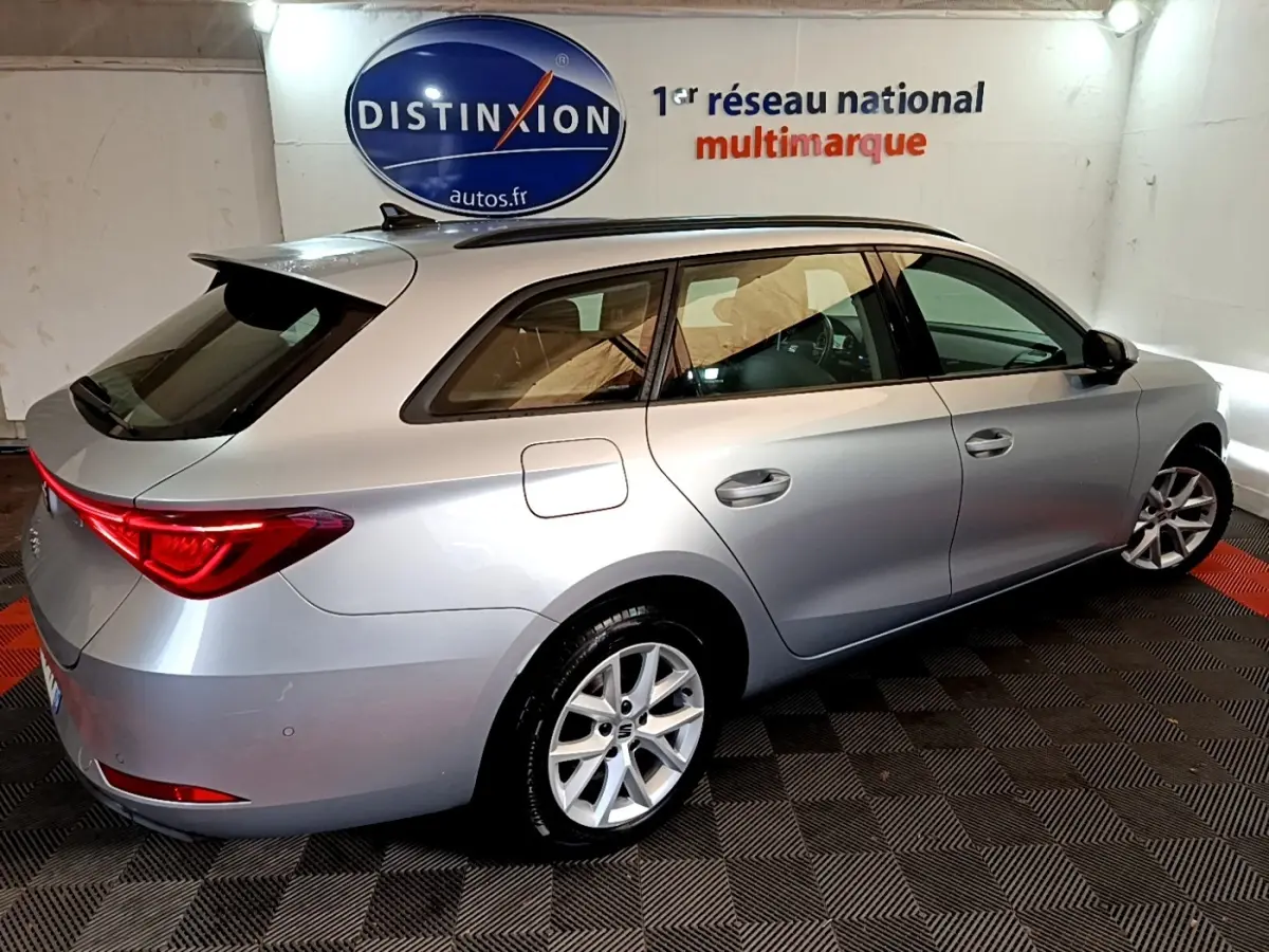 SEAT LEON gris clair en break vu de 3/4 arrière droit dans un showroom avec logo Distinxion en arrière-plan.