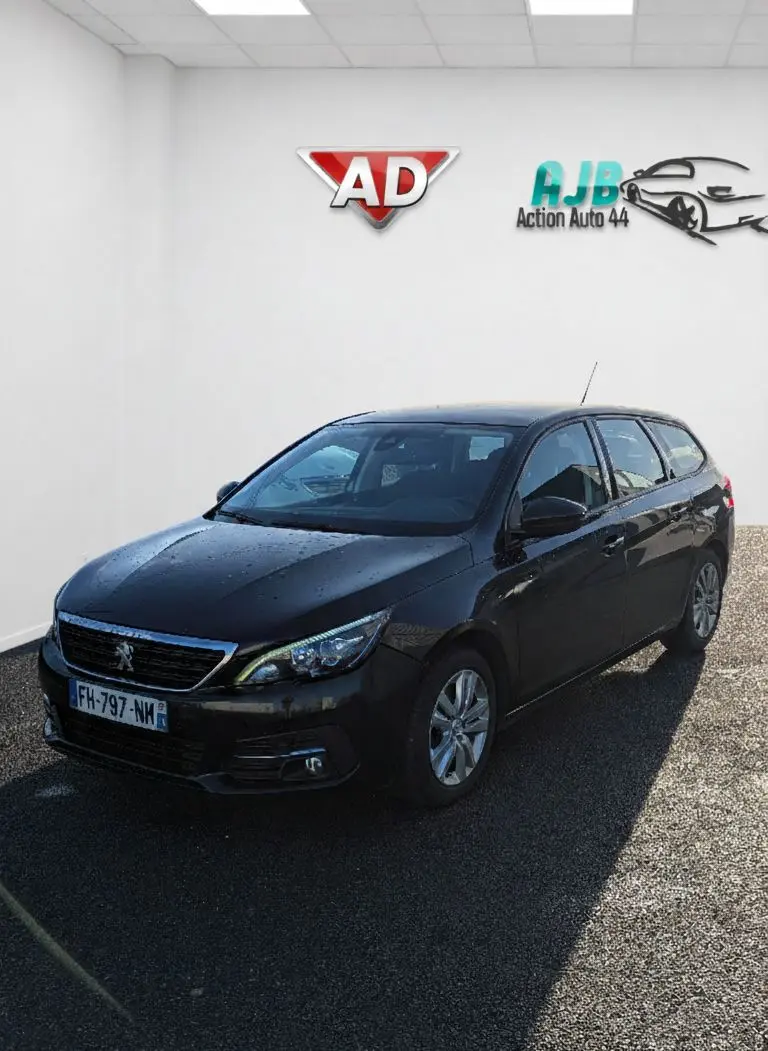 Peugeot 308 SW noire vue en 3/4 avant droit, avec jantes alu et calandre chromée visible.