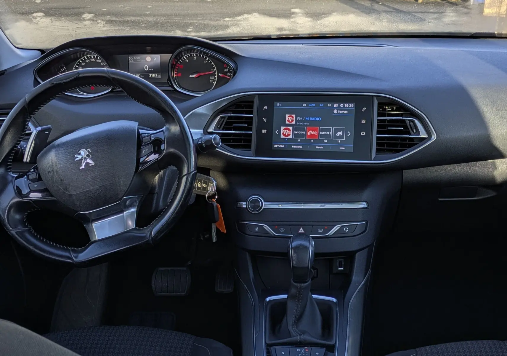 Vue intérieure avant de la Peugeot 308 SW noire, montrant le tableau de bord avec écran tactile et volant cuir.