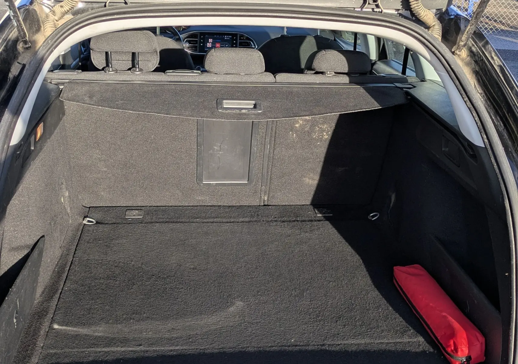 Coffre ouvert d'une Peugeot 308 SW noire, vue arrière montrant l'espace de chargement et un triangle de sécurité rouge.