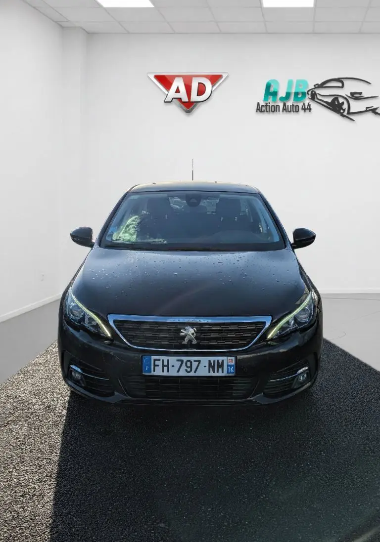 Vue avant d'une Peugeot 308 SW noire 2019 avec phares allumés et logo lion visible sur la calandre.