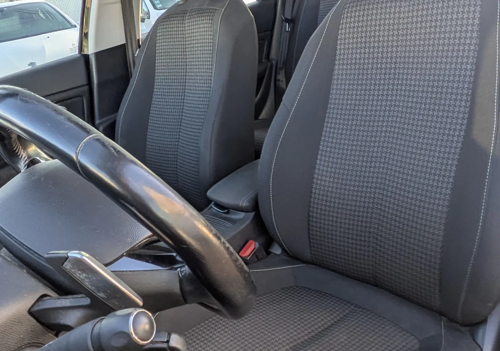 Vue intérieure côté conducteur de la Peugeot 308 SW 2019, sièges tissu noir avec motifs et toit ouvrant panoramique.