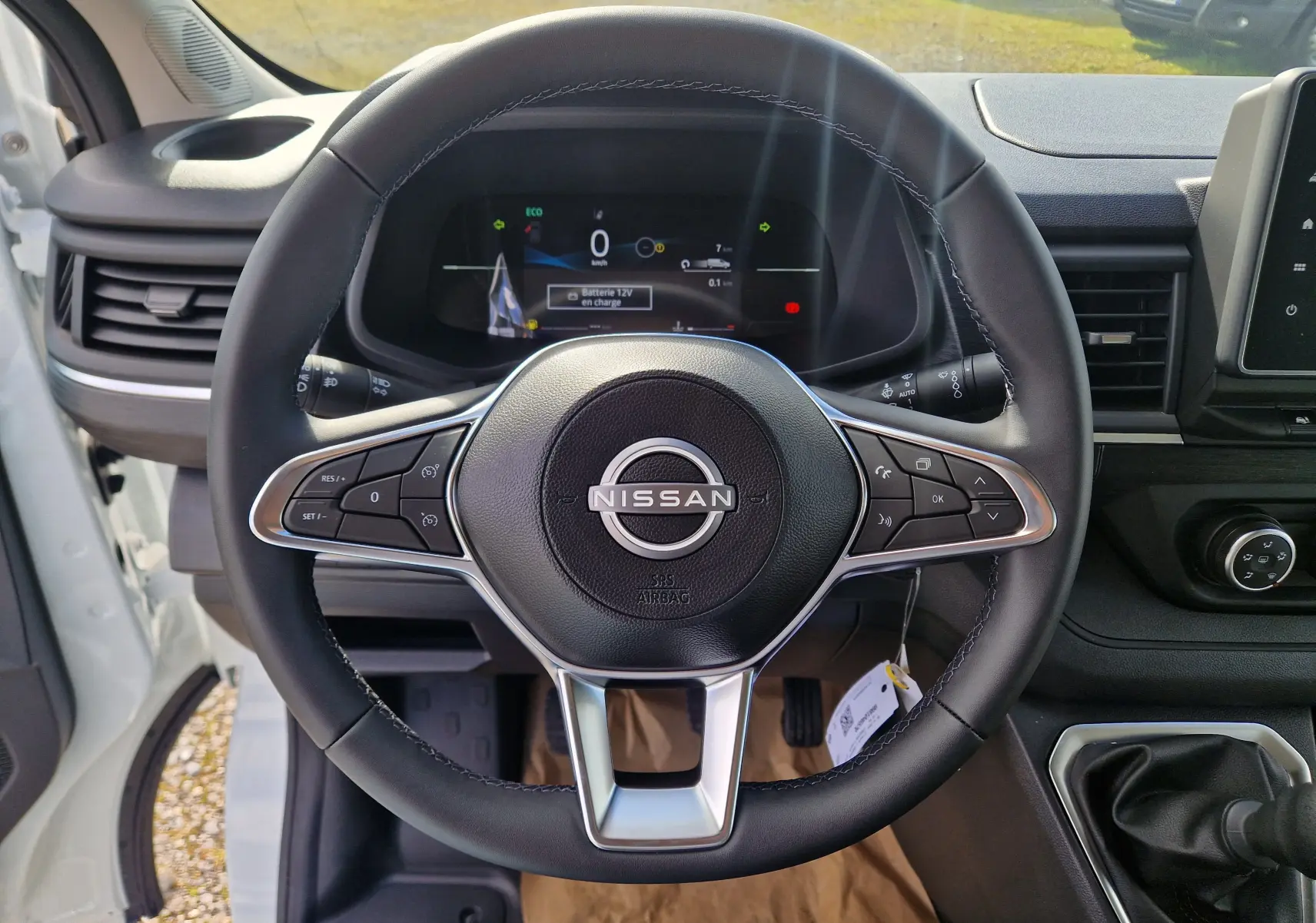 Vue intérieure centrée sur le volant noir du Nissan Primastar blanc 2025 avec tableau de bord digital et levier de vitesses manuel.