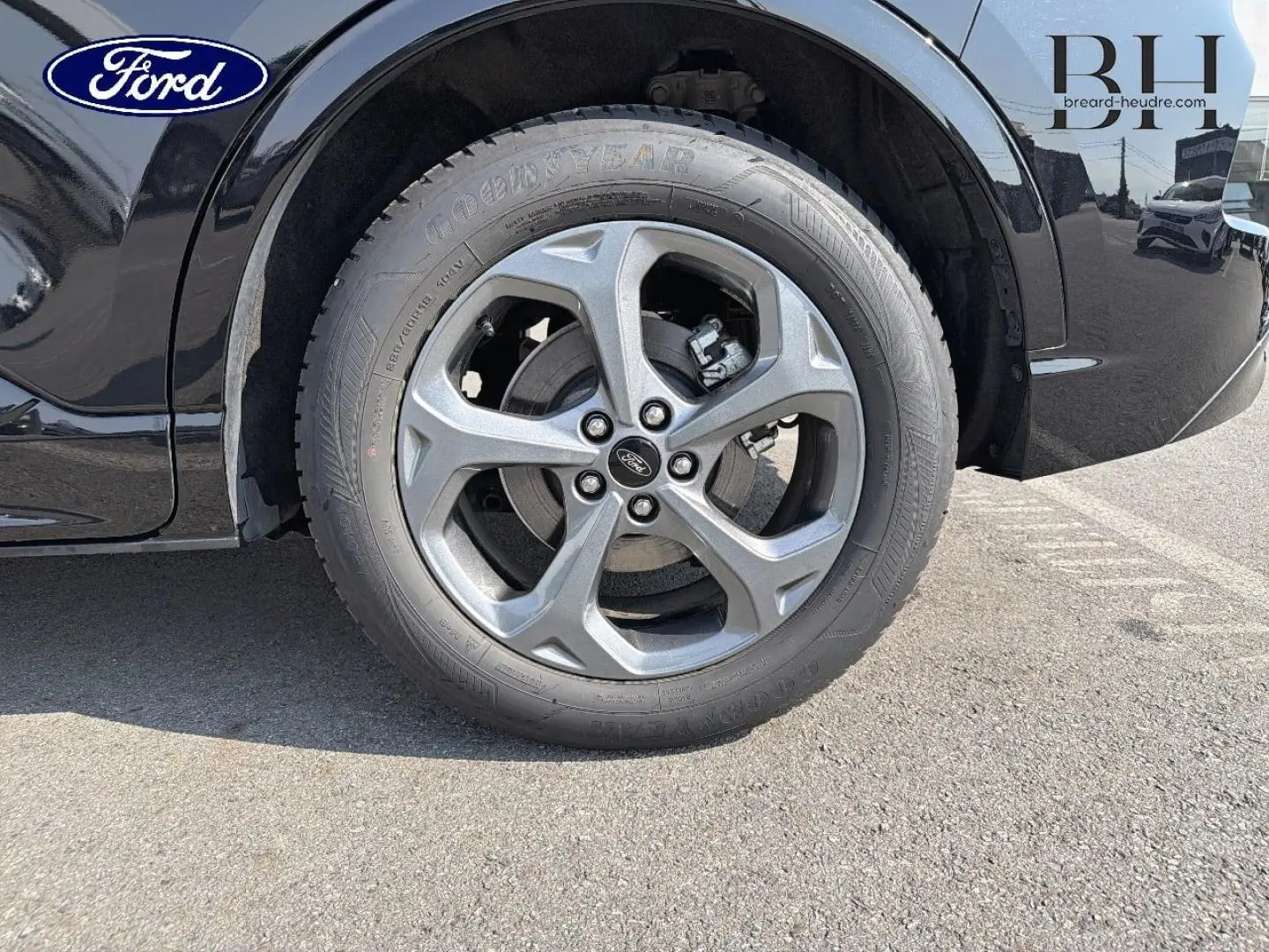 Gros plan sur la roue avant droite du Ford Kuga noir Agate Métallisée, mettant en valeur la jante alu et le logo Ford.