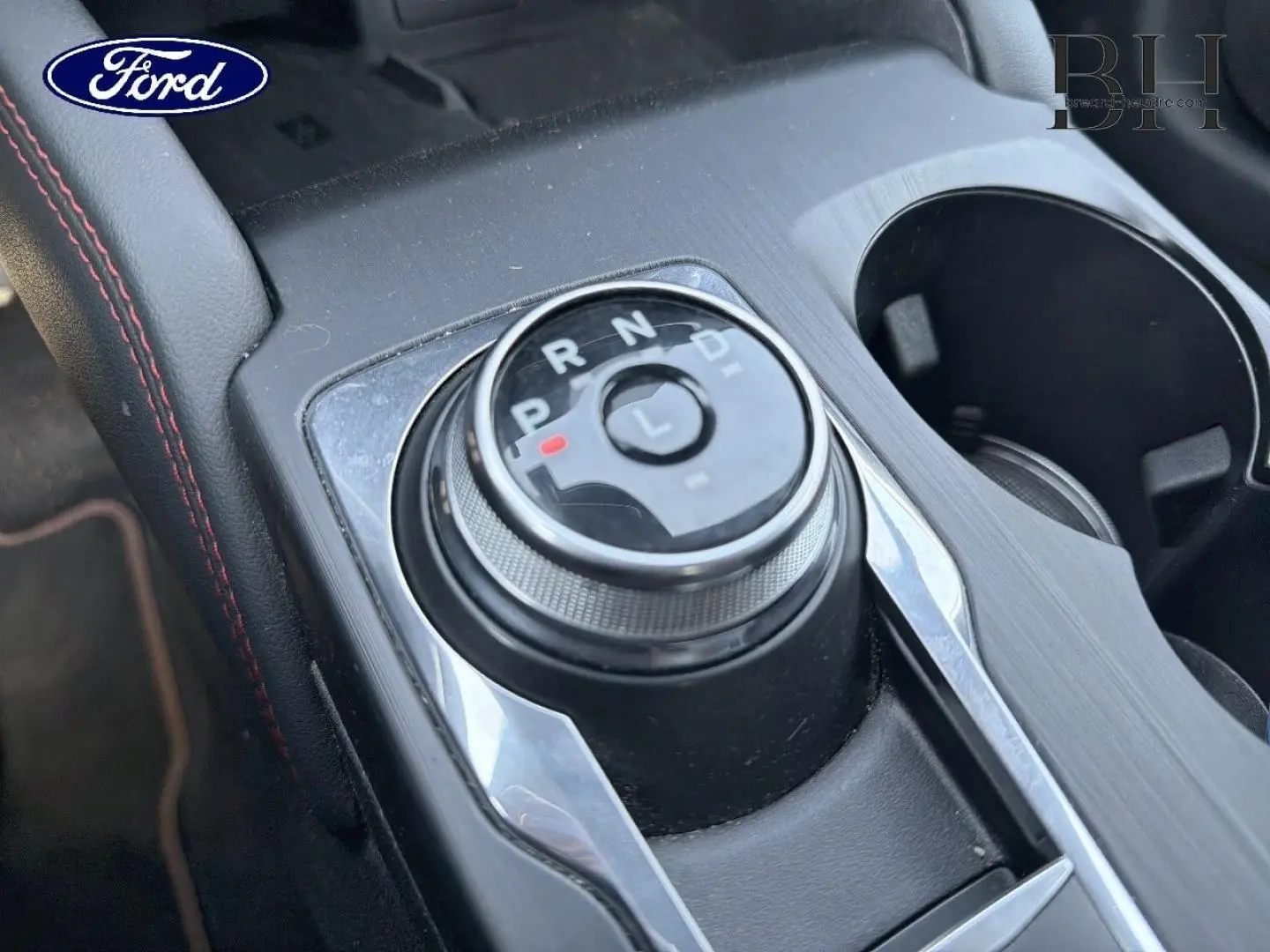 Gros plan sur la molette de sélection de la boîte automatique du Ford Kuga noir avec surpiqûres rouges, console centrale visible.