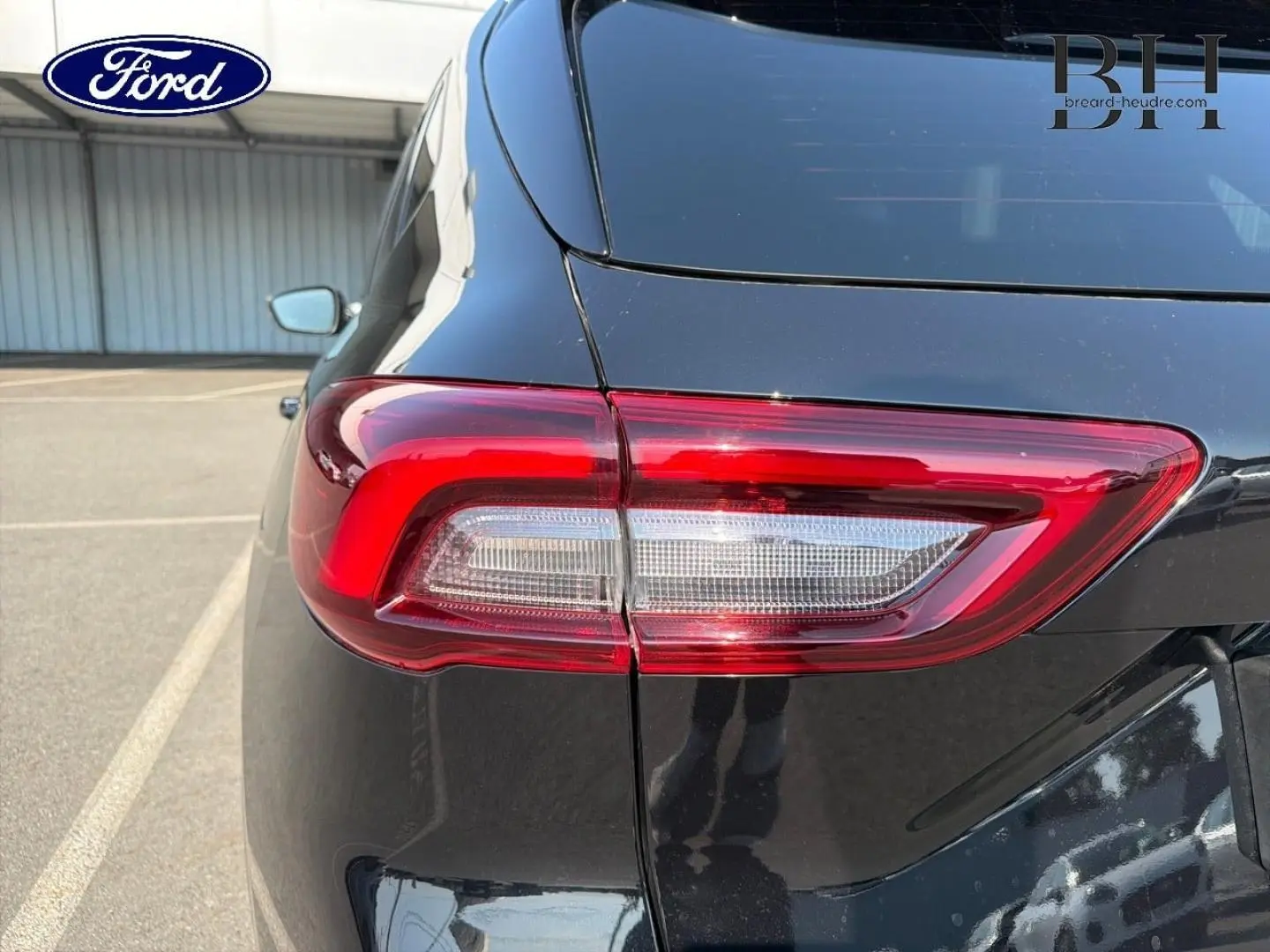 Gros plan sur le feu arrière gauche d’un Ford Kuga noir Agate Métallisée, avec reflet sur la carrosserie lisse.