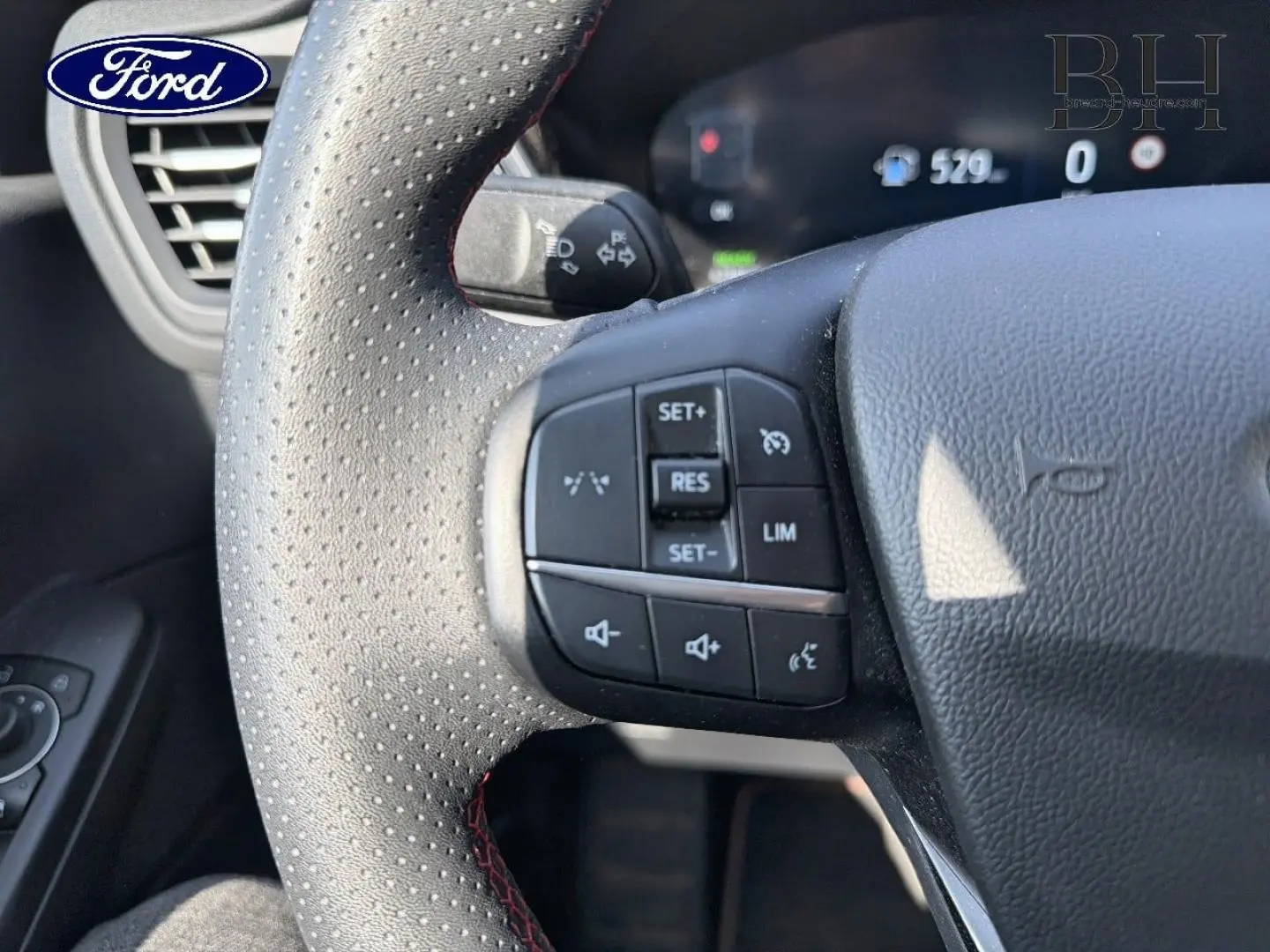 Gros plan sur le volant perforé avec commandes multifonctions du Ford Kuga 2025 noir Agate Métallisé.