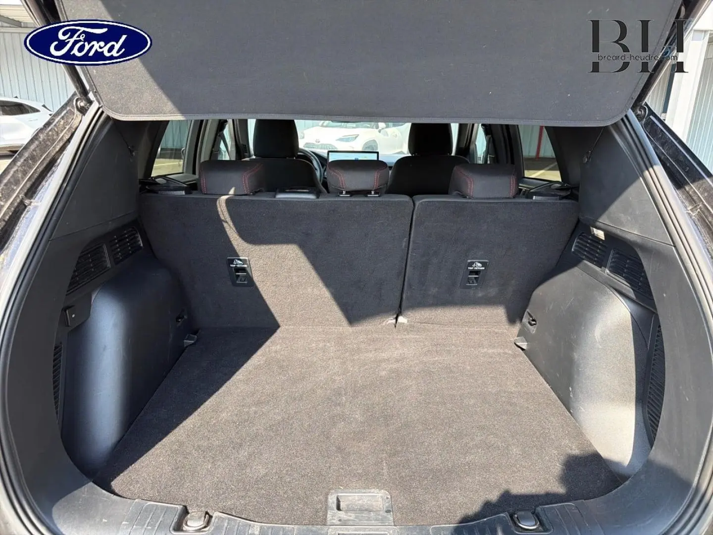 Coffre ouvert vu de l'arrière du Ford Kuga 2025, montrant un espace de chargement spacieux et tapis noir.