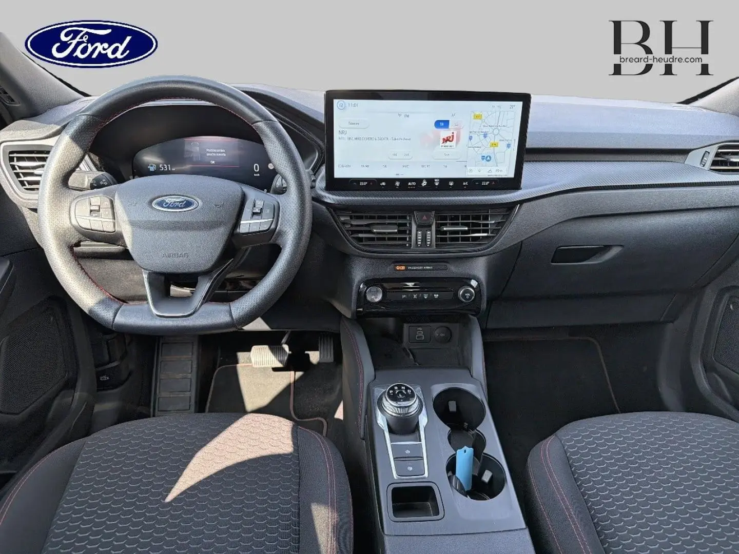 Vue intérieure avant du Ford Kuga 2025, tableau de bord noir avec écran tactile large et volant multifonction.