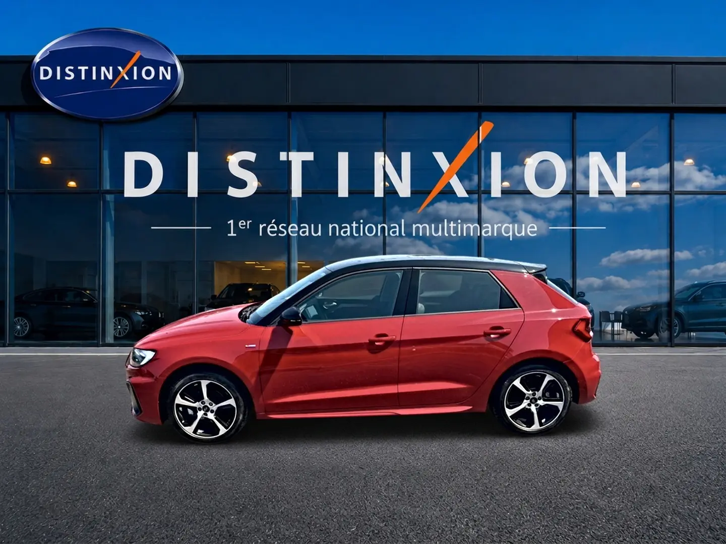 Profil droit d'une Audi A1 Sportback 30 TFSI rouge toit noir avec jantes alu et becquet arrière, devant une vitrine Distinxion.