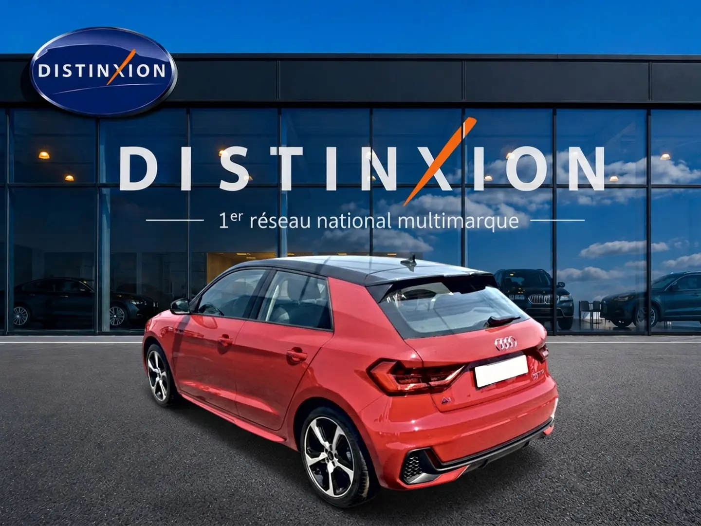 Audi A1 Sportback rouge et noir vue 3/4 arrière droit, avec jantes alu et toit contrasté noir devant vitrine Distinxion.