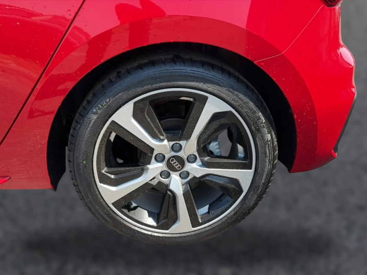 Gros plan sur la roue arrière droite d'une Audi A1 Sportback rouge, mettant en valeur la jante alu bicolore et le logo Audi.