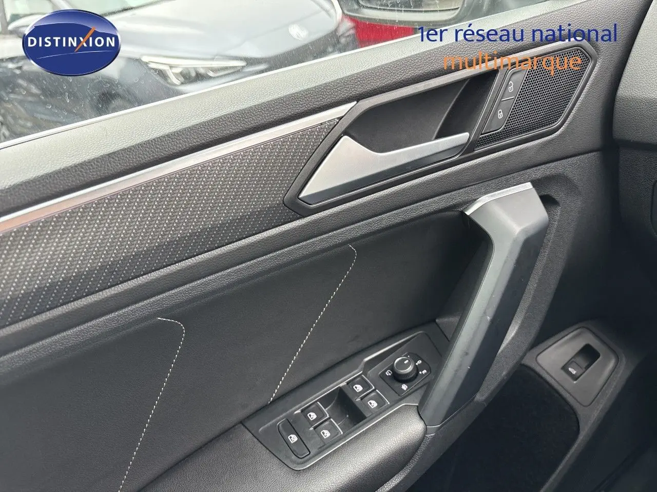 Détail de la porte avant gauche du Volkswagen Tiguan 2024 en intérieur noir avec commandes des vitres et poignée angulaire.