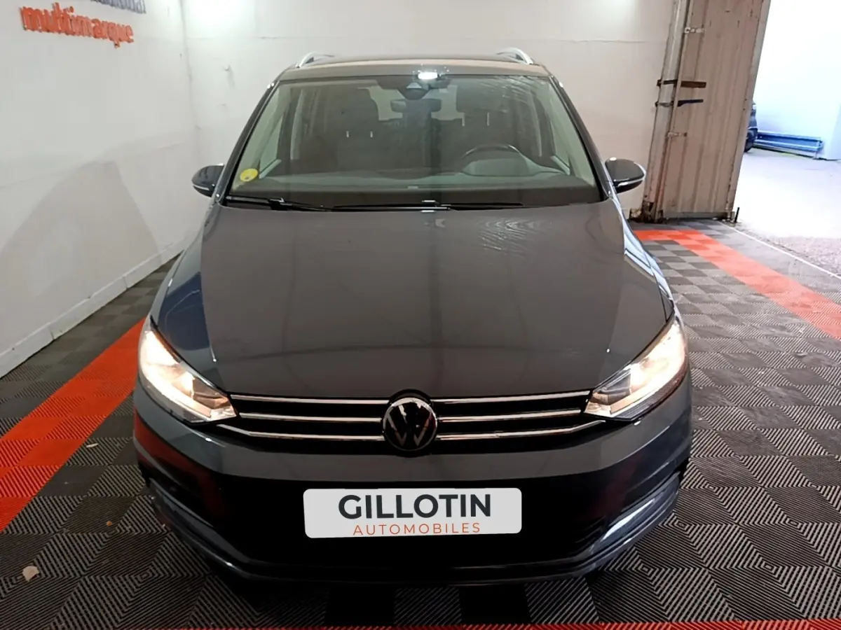 Vue avant d'un Volkswagen Touran gris foncé 2023 avec phares allumés dans un garage fermé.