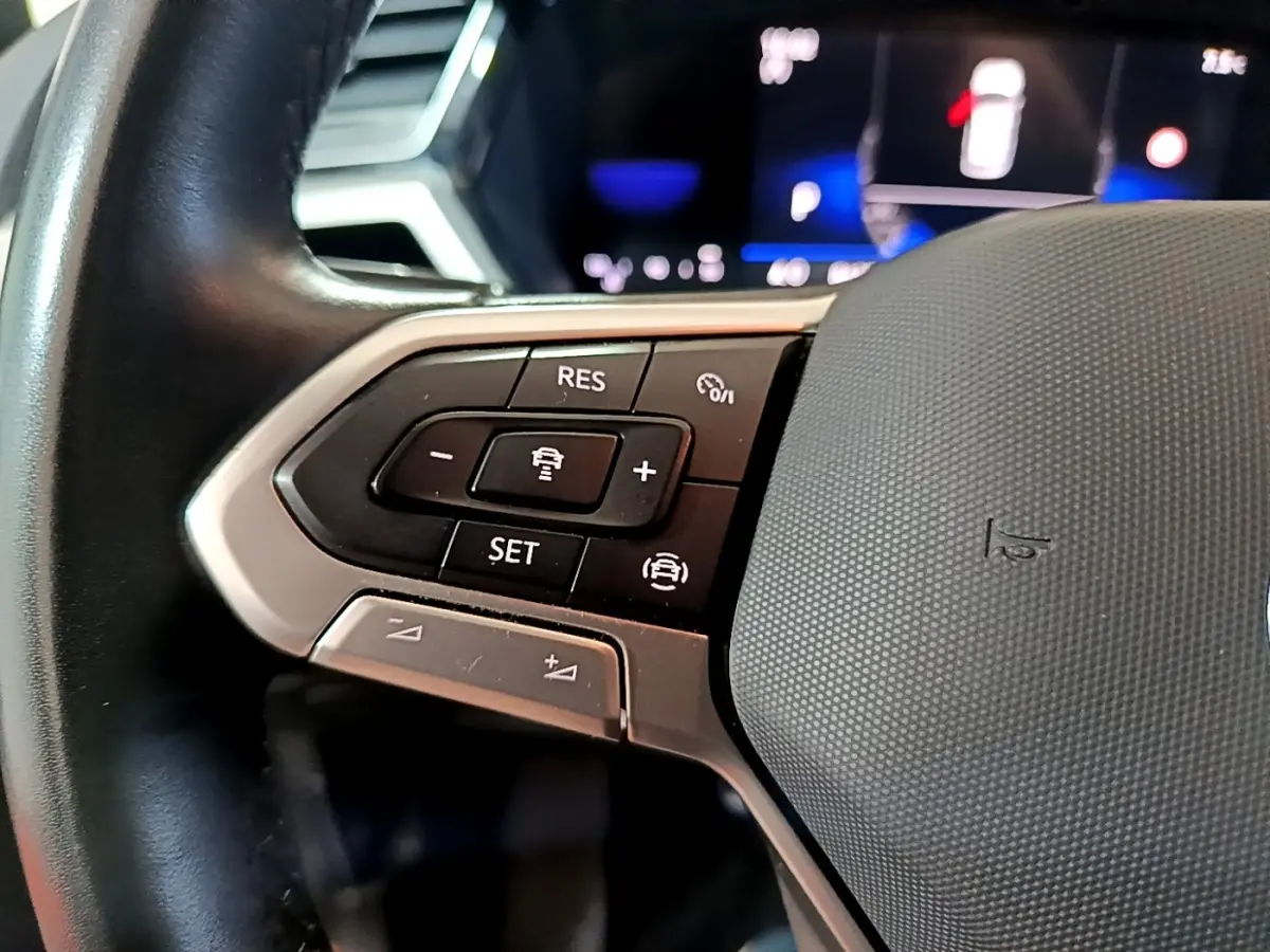 Gros plan sur les commandes du volant cuir noir du Volkswagen Touran 2023, version 2.0 TDI gris foncé.