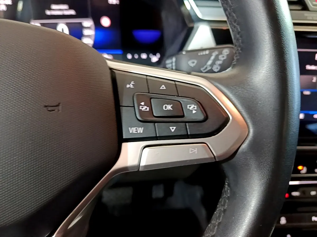 Gros plan sur les commandes du volant cuir noir du Volkswagen Touran gris foncé 2023, avec affichage digital en arrière-plan.