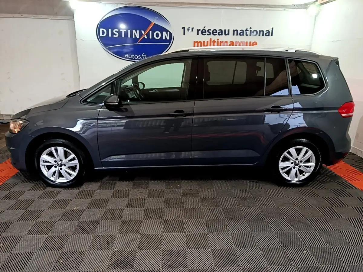 Profil côté gauche d'un Volkswagen Touran gris foncé 2023 stationné en intérieur avec jantes alliage visibles.