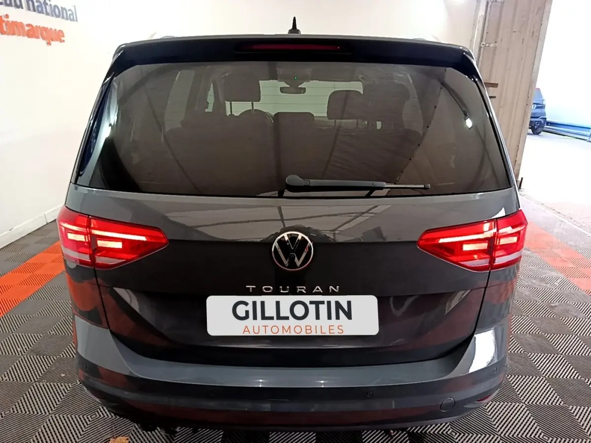 Vue arrière d'un Volkswagen Touran gris foncé 2023 avec feux LED allumés et logo VW visible.