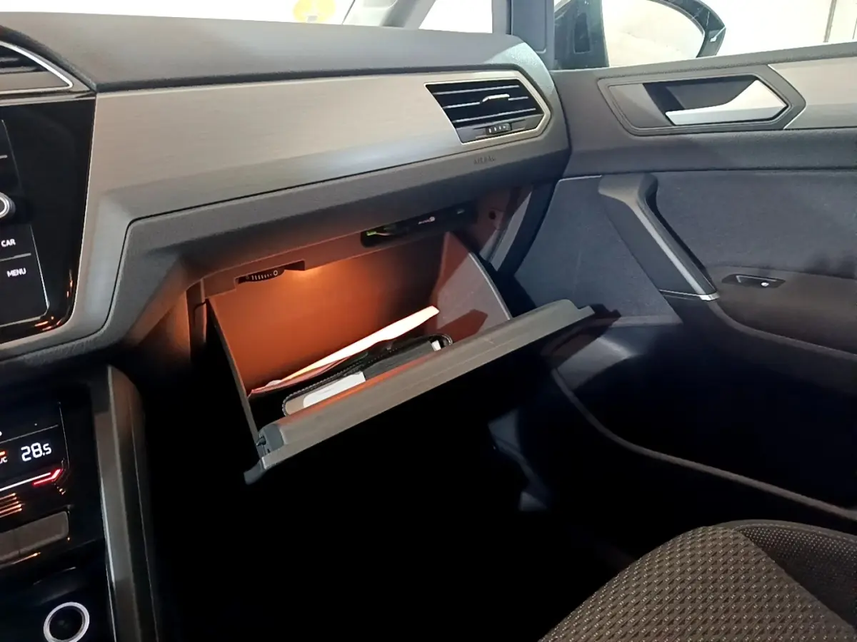 Intérieur du Volkswagen Touran 2023 gris foncé, vue côté passager avec boîte à gants ouverte et éclairage intérieur.