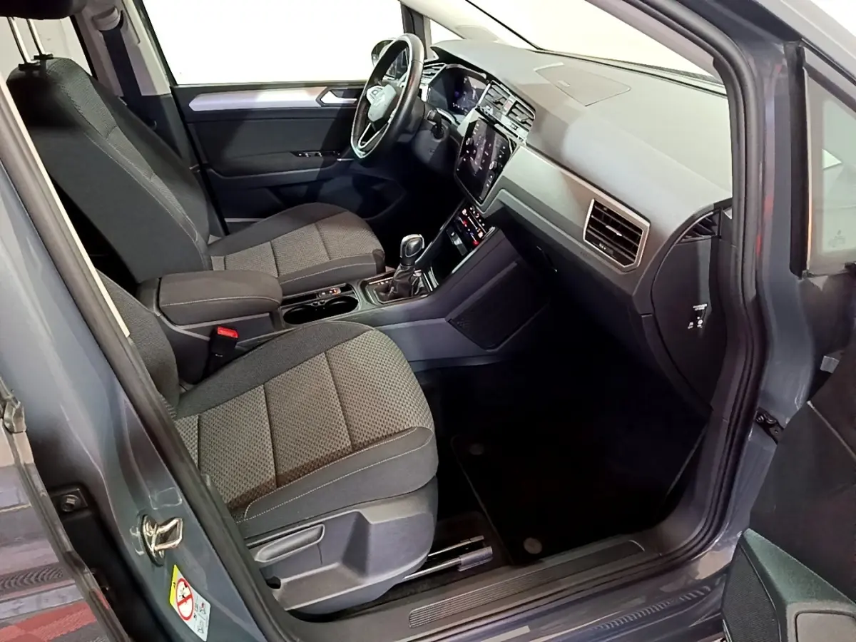 Intérieur avant droit du Volkswagen Touran gris foncé 2023, sièges tissu et tableau de bord avec écran tactile.