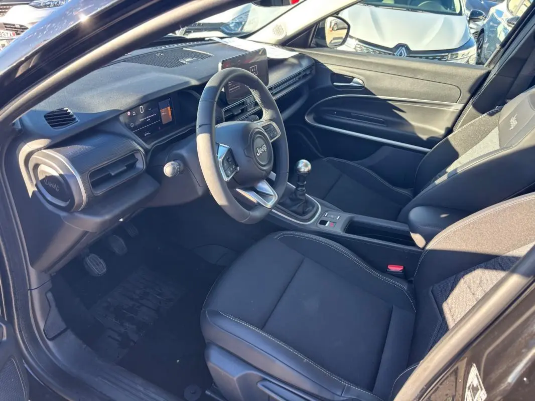 Vue intérieure côté conducteur du Jeep Avenger noir 2024, avec volant multifonction, boîte manuelle et sièges tissu noirs.