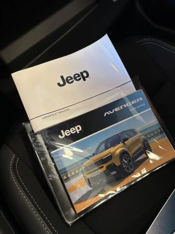 Vue rapprochée des manuels Jeep posés sur un siège noir avec surpiqûres blanches, sans véhicule visible.
