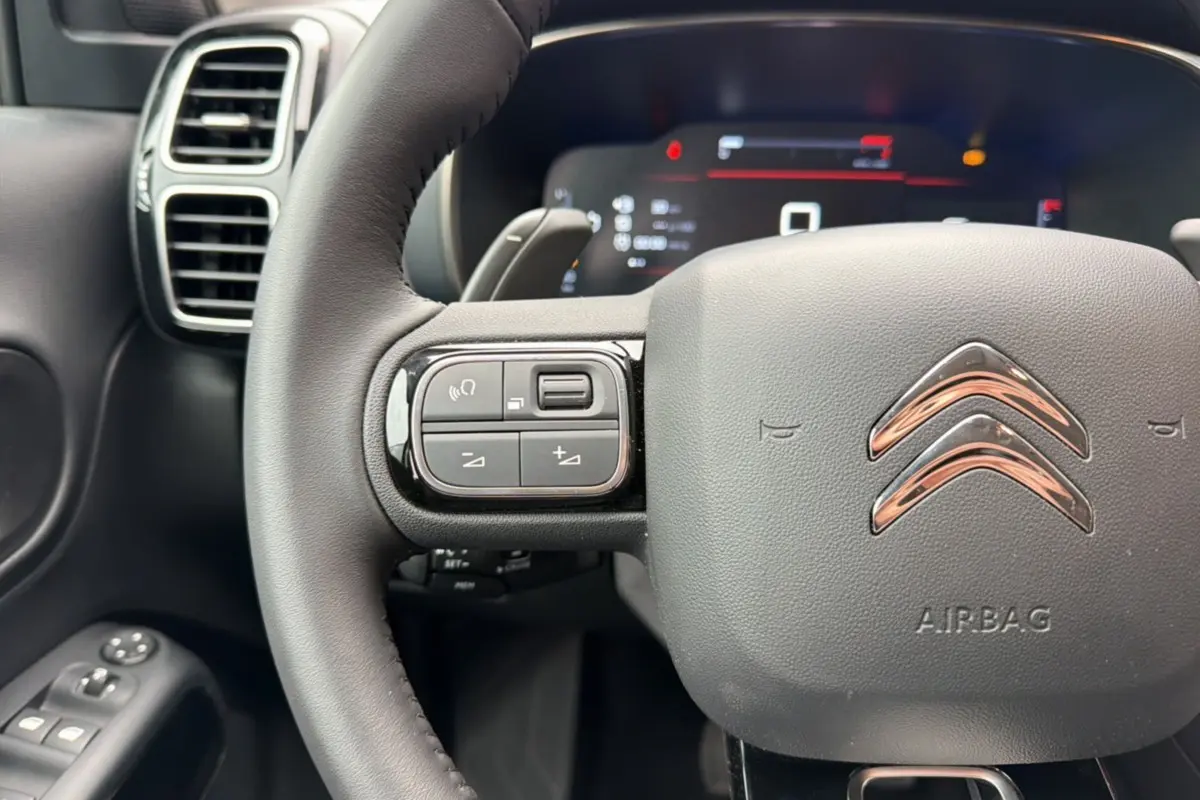 Gros plan sur le volant cuir multifonctions noir du Citroën C5 Aircross 2025 avec commandes intégrées et tableau de bord numérique flou.