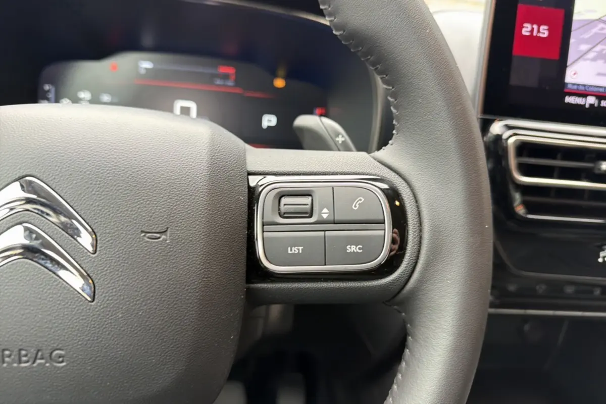 Gros plan sur le volant cuir noir du Citroën C5 Aircross 2025, avec commandes multifonctions et tableau de bord numérique en arrière-plan.