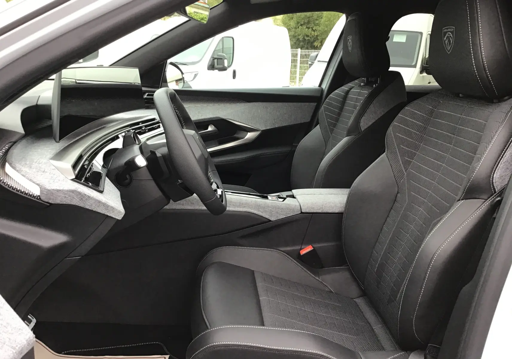 Vue intérieure côté conducteur du Peugeot 3008 2026, sièges noirs avec logo Peugeot brodé sur les appuie-têtes.