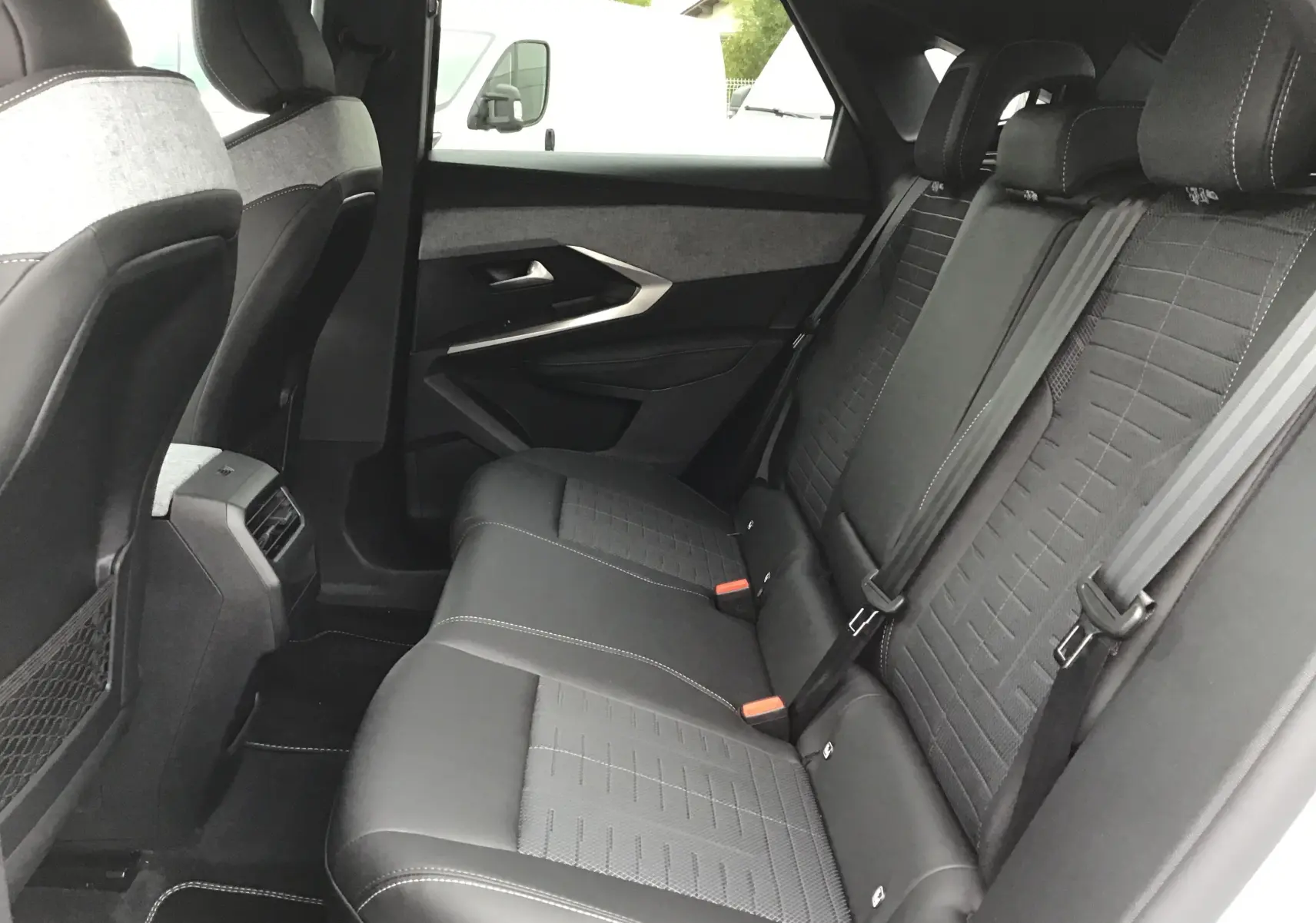 Vue intérieure arrière côté droit du Peugeot 3008 1.2 Hybrid 145 GT+ blanc Okenite avec sièges noirs en tissu et cuir, appuie-têtes visibles.