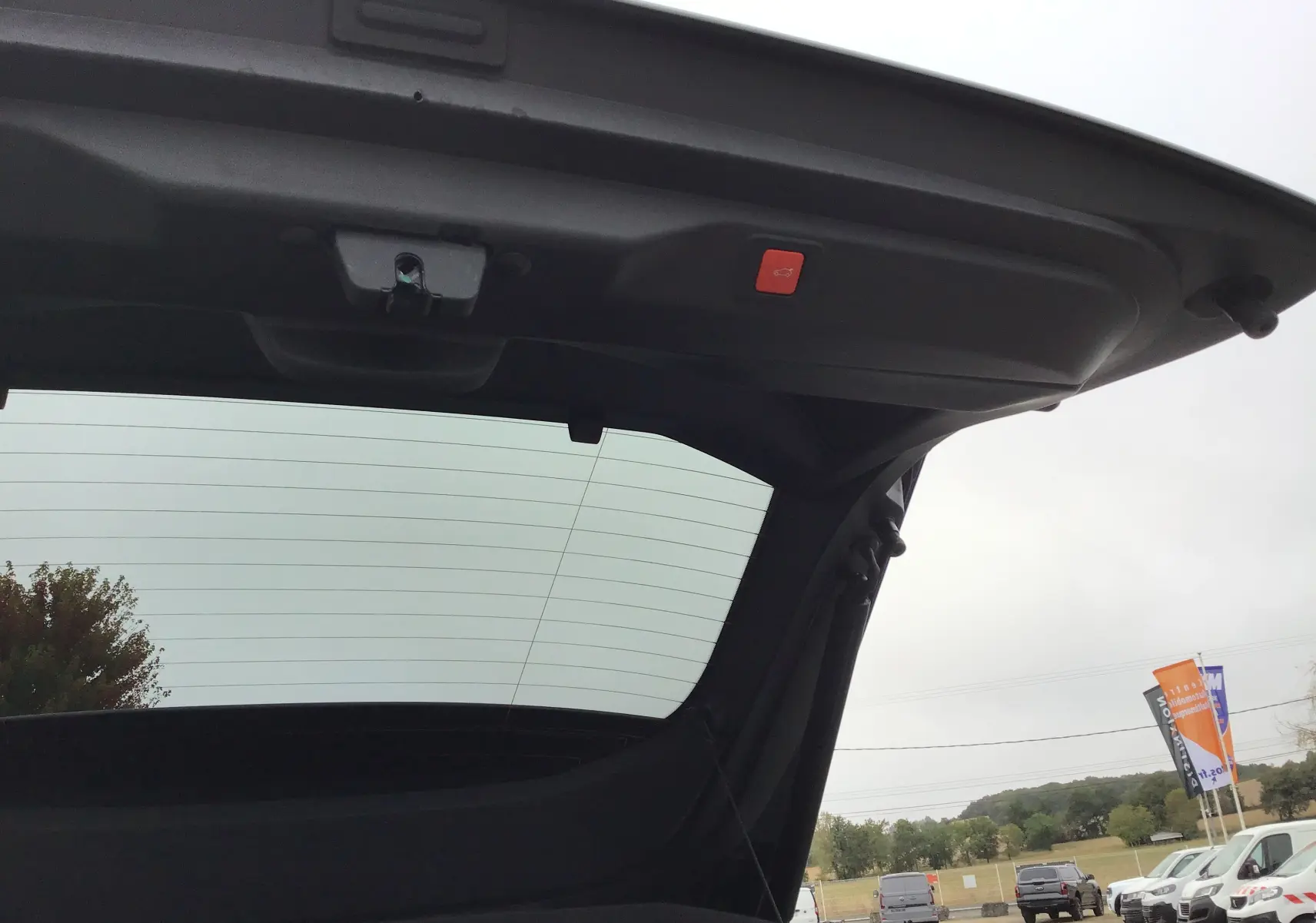 Vue intérieure du hayon ouvert du Peugeot 3008 blanc Okenite, mettant en valeur la lunette arrière et le bouton de fermeture électrique.