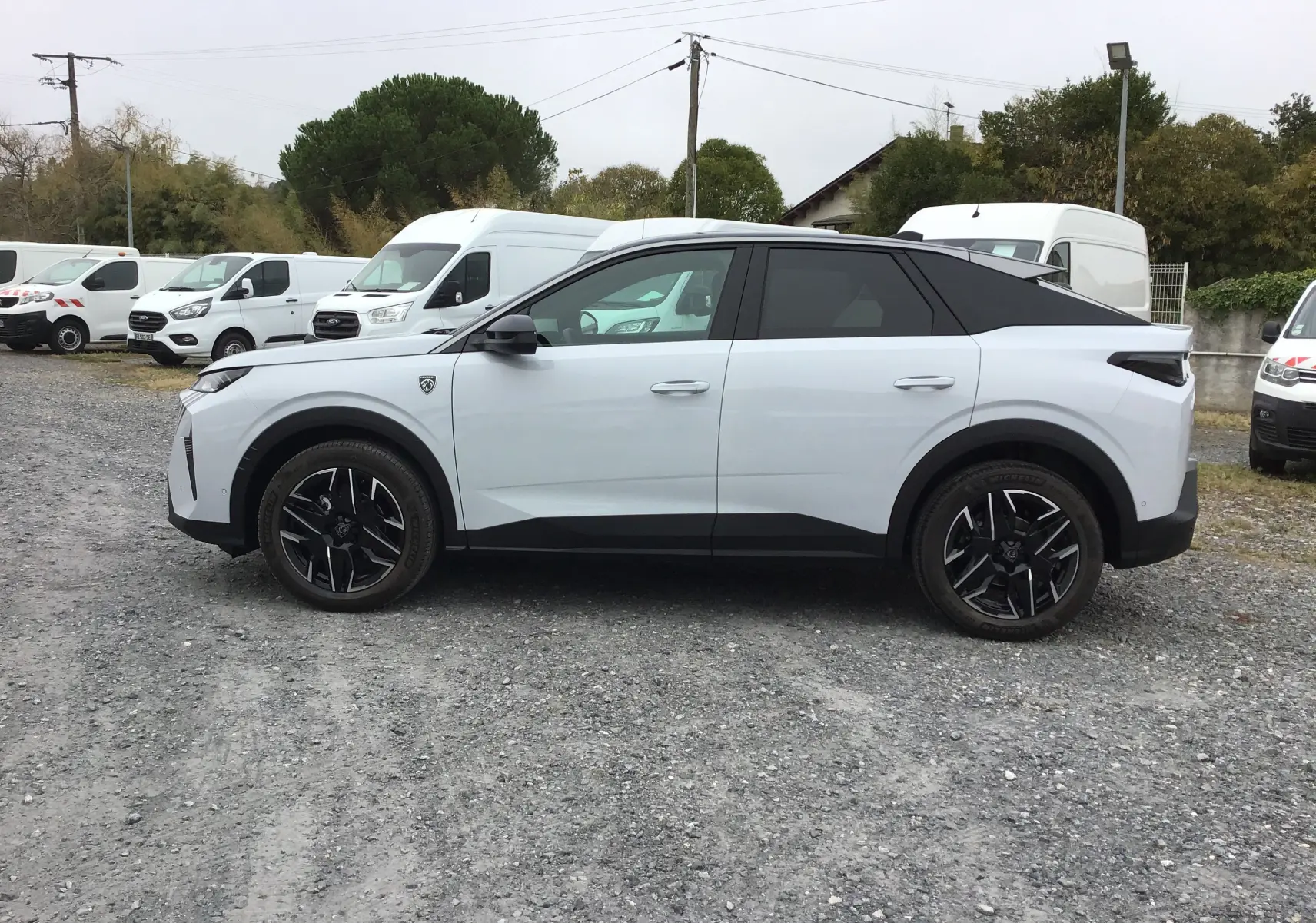 Profil droit du Peugeot 3008 blanc Okenite avec toit noir, jantes noires et détails modernes sur un sol gravillonné.