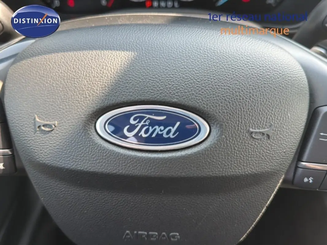 Gros plan sur le volant noir avec logo Ford bleu au centre d'une Ford Focus SW 2022, finition Titanium X Business.